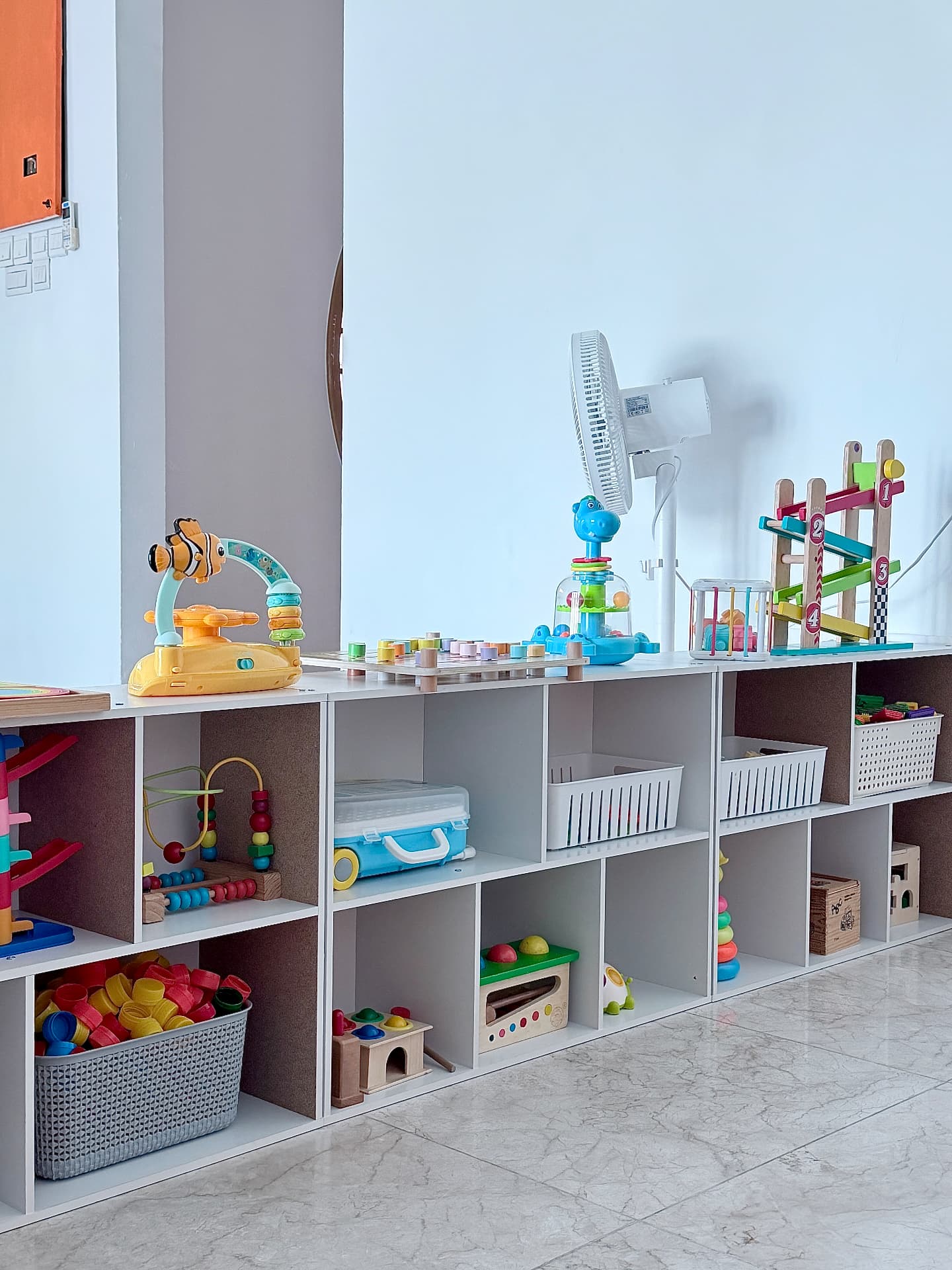 Low open shelving filled with wooden and colourful learning toys along a bright wall.