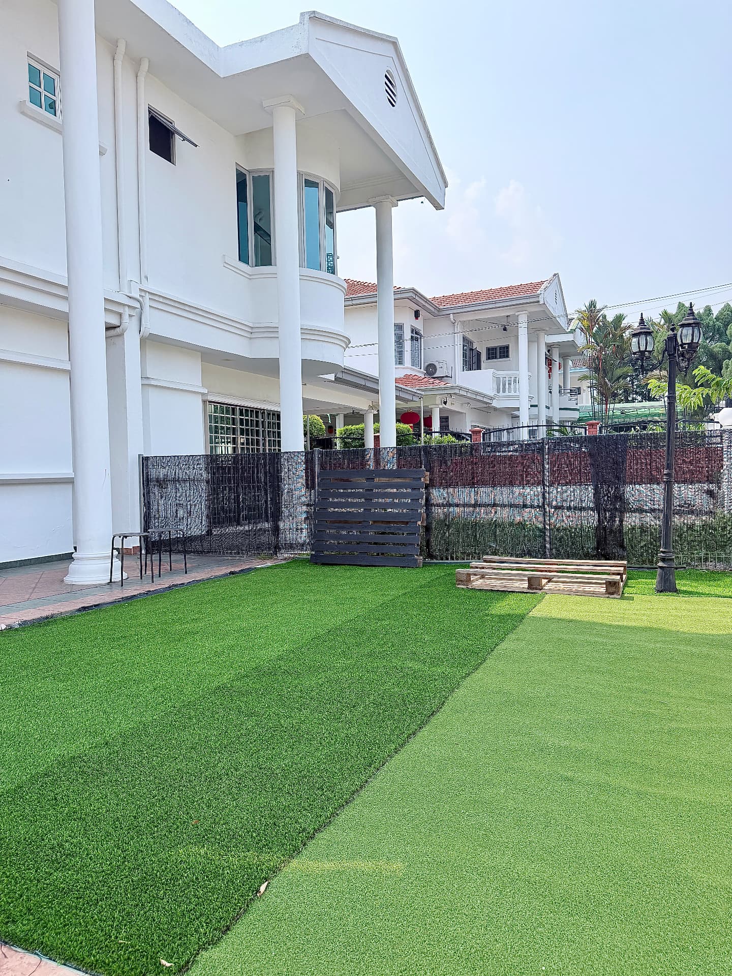A wide outdoor lawn beside the centre building with a fence and shade.