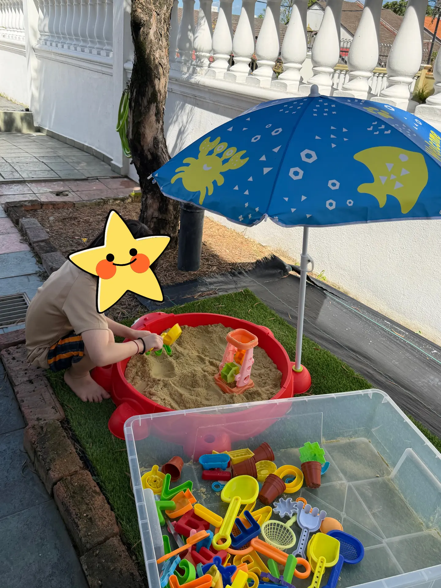 A child scooping sand in an outdoor sand tray under a shade umbrella.