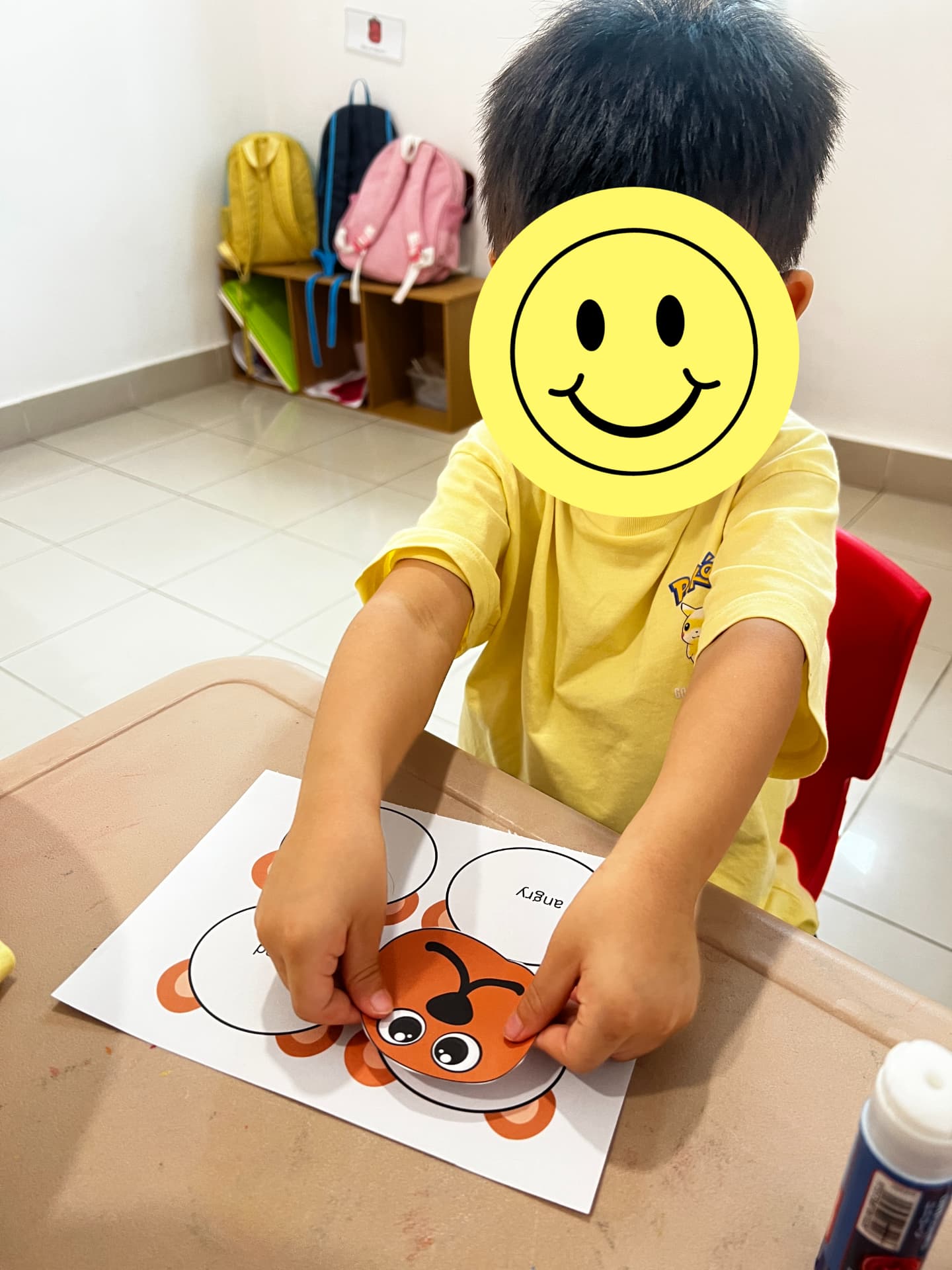 A child sticking a paper face onto a feelings activity sheet.