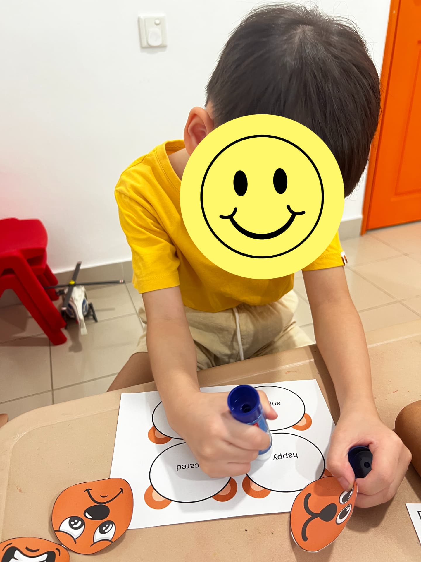 A child gluing paper faces onto a feelings worksheet.
