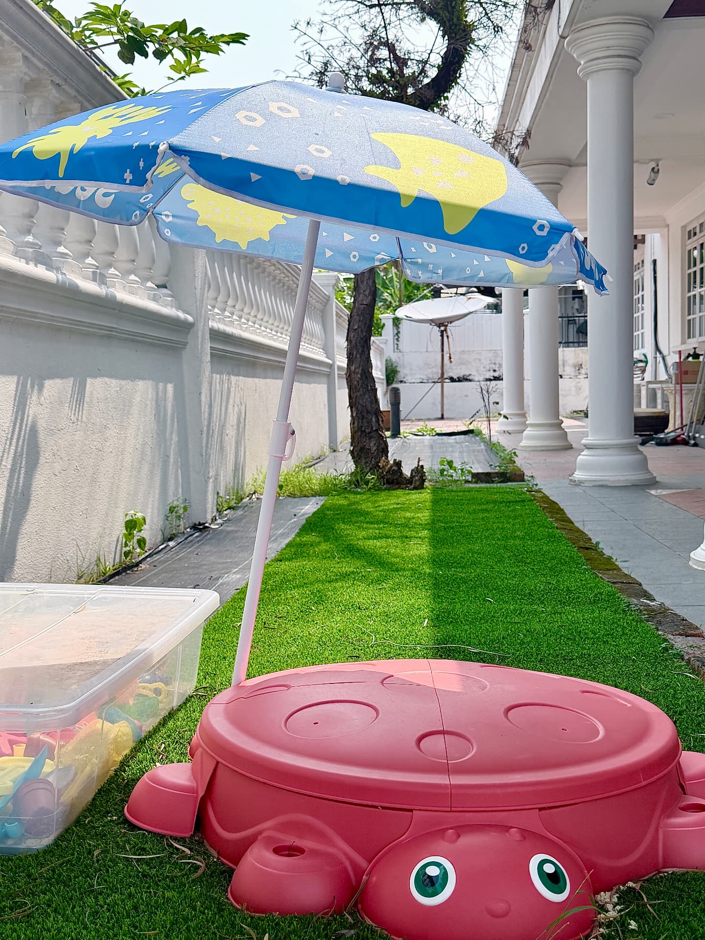 A crab-shaped sand tray with a bright umbrella on the outdoor artificial lawn.