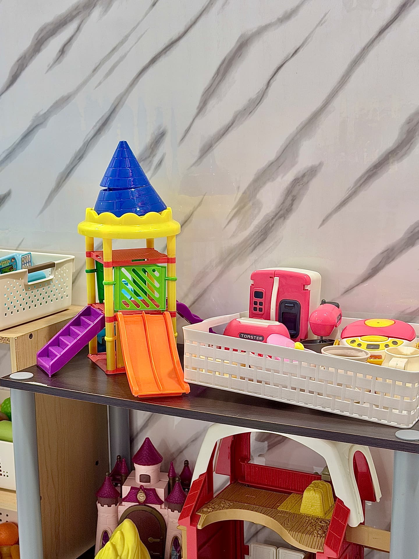 A shelf with a toy playground set, dollhouse and pretend kitchen accessories.