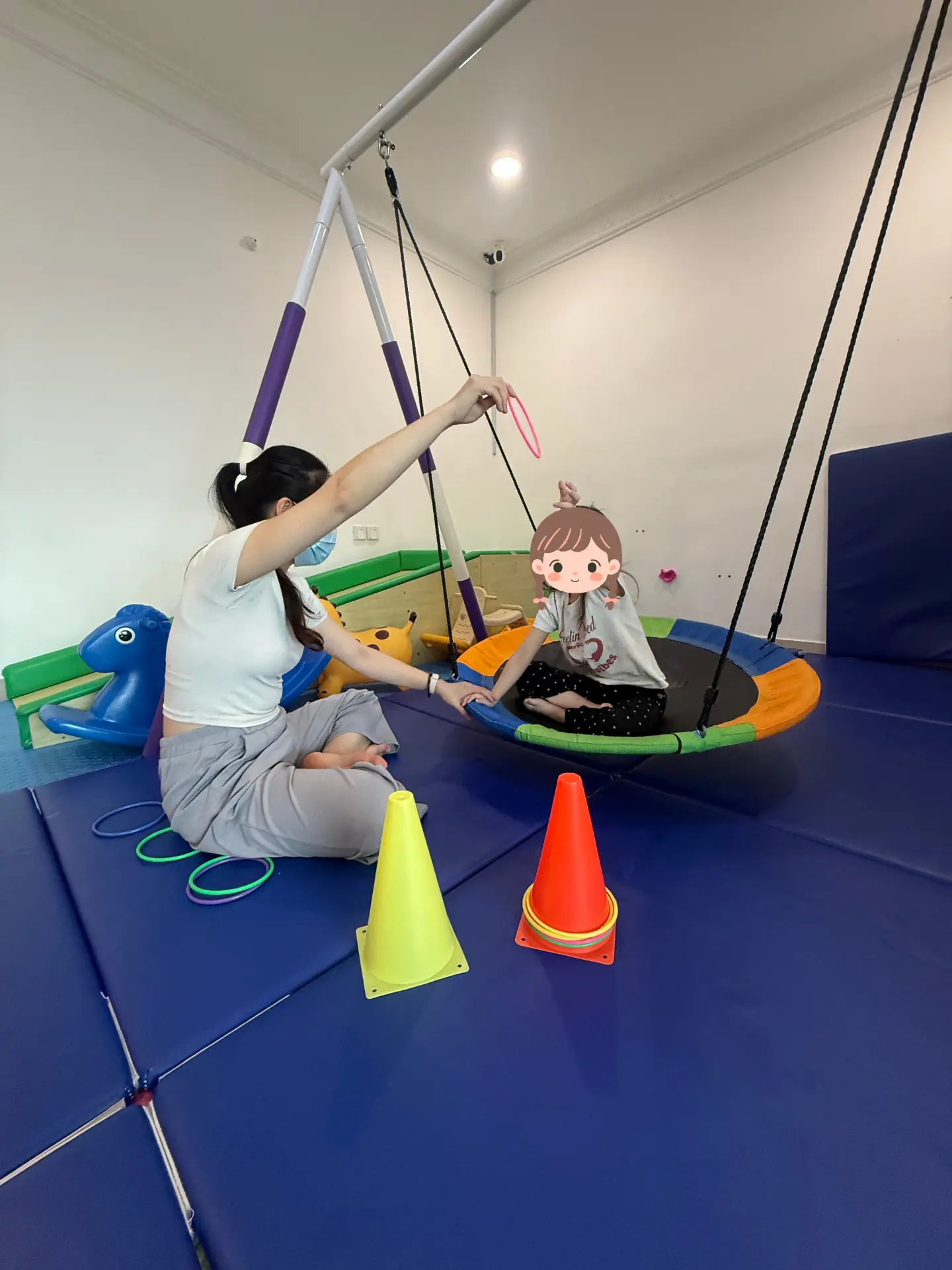 A therapist and child doing sensory swing activities with rings and cones.