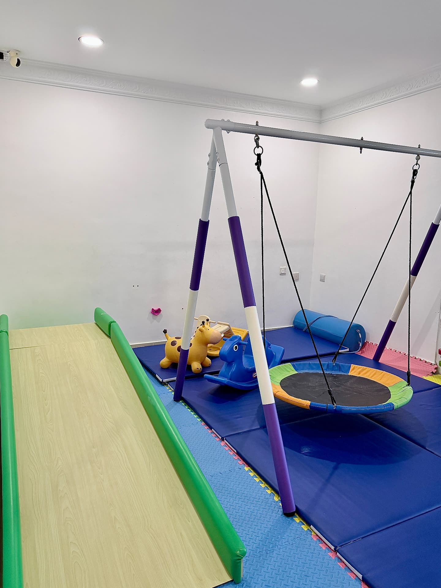 An indoor therapy gym with a swing, slide, trampoline, and soft mats.
