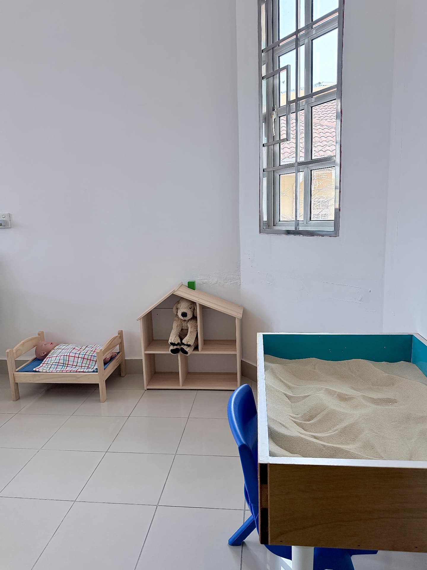 A quiet corner with a doll house, sand tray, and small wooden bed.