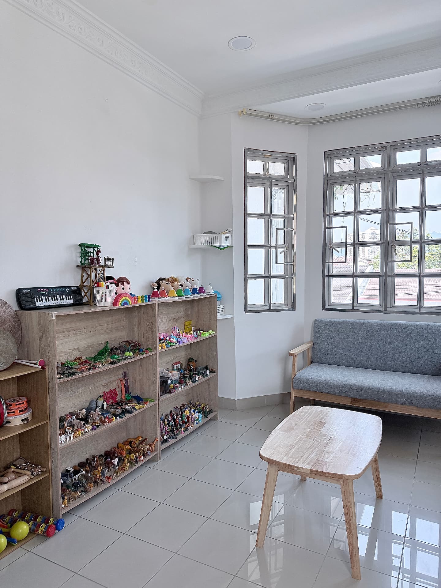 A bright therapy room with toy shelves, a sofa, and large windows.