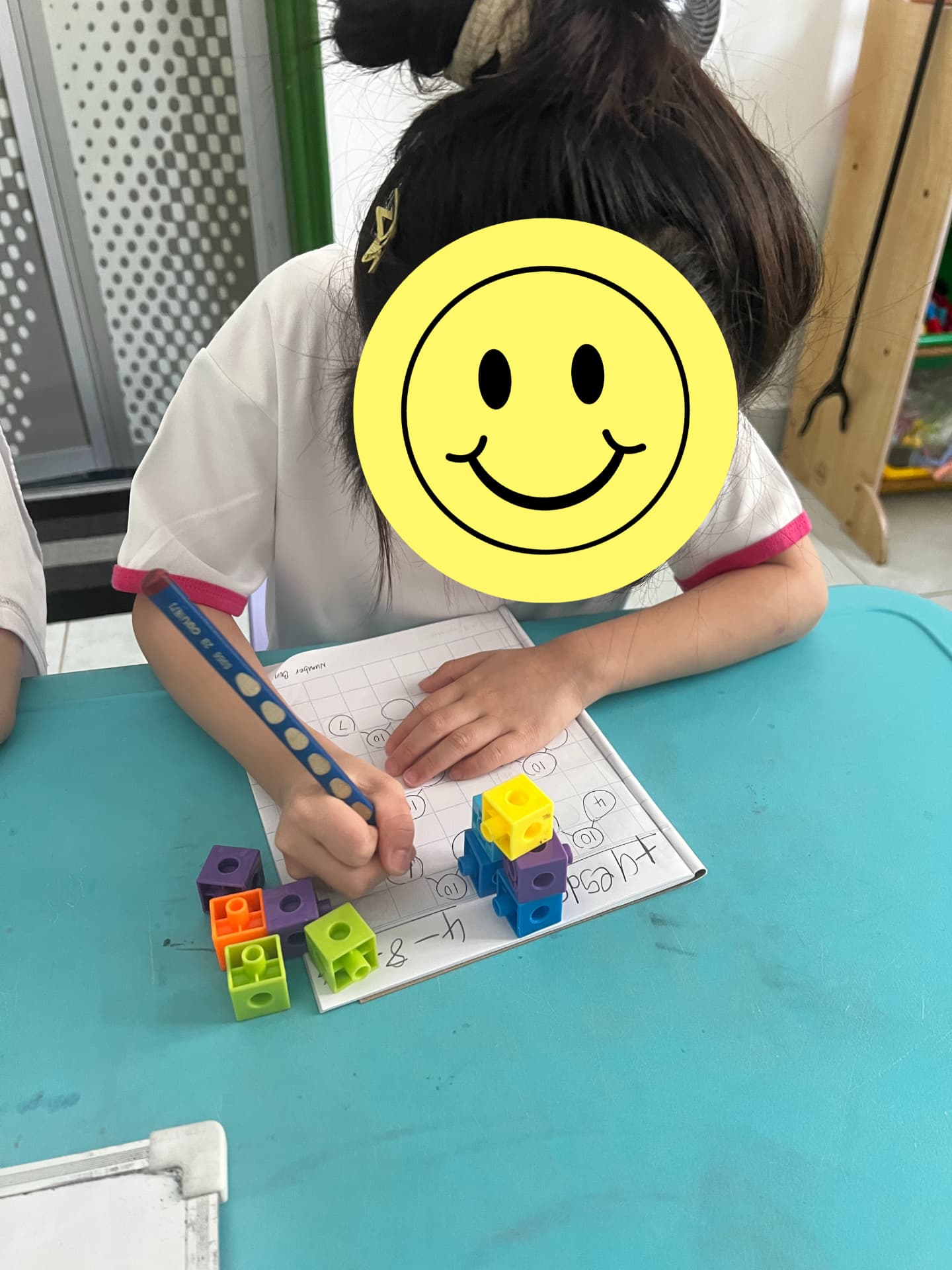 A child writing numbers in a workbook with colourful counting cubes.