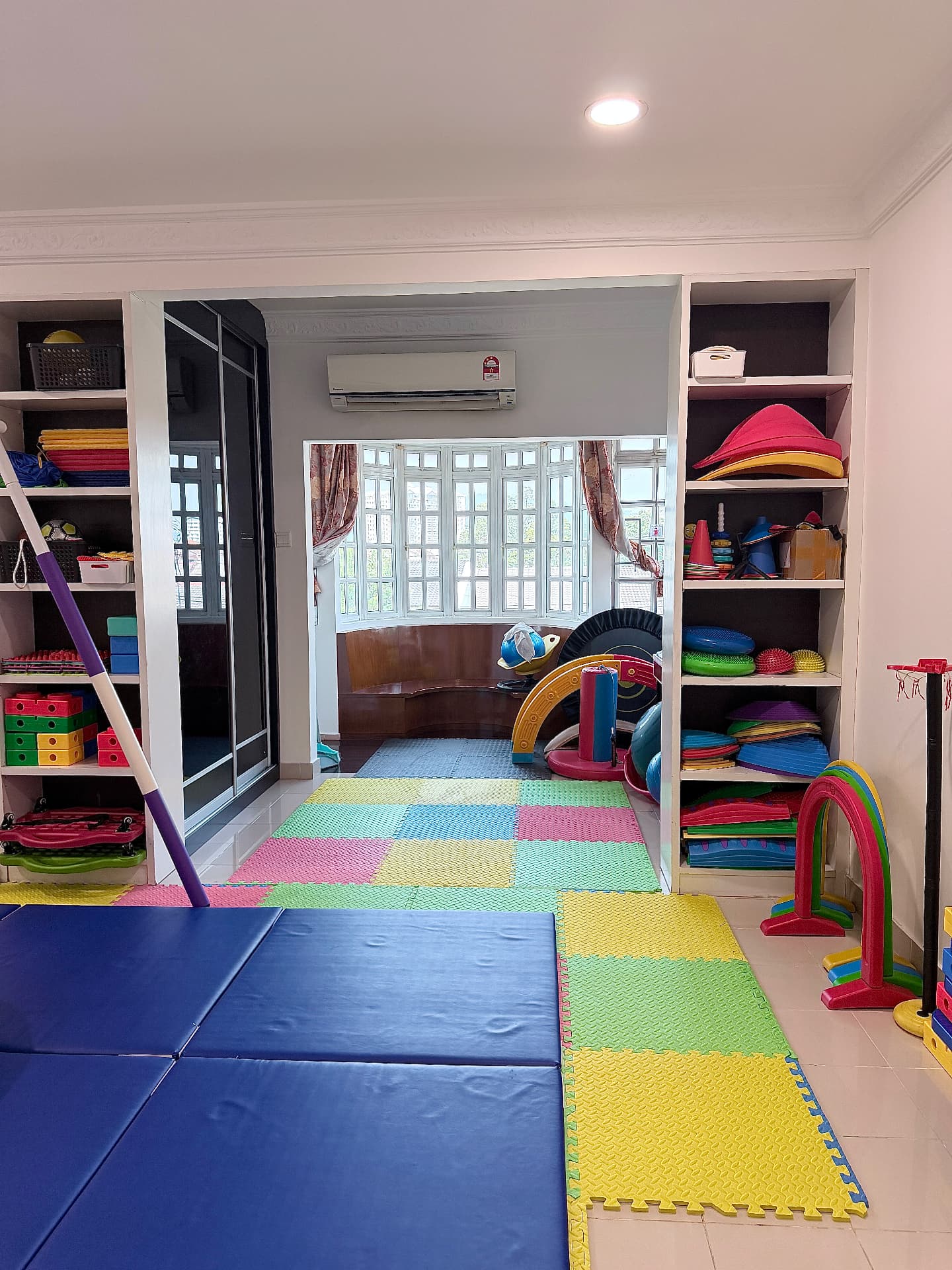 A colourful therapy and play room with mats, shelves of toys, and gym equipment.