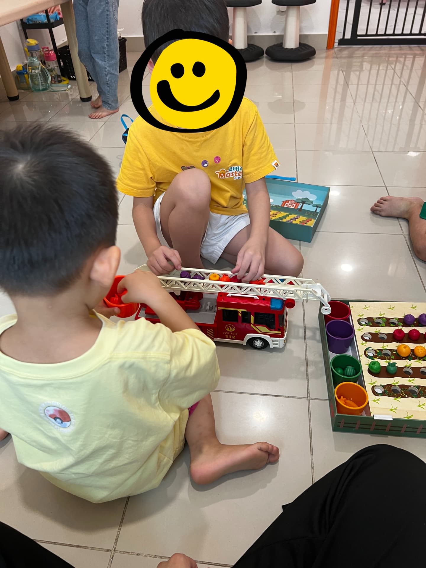 Two children playing together with a toy fire truck and sorting game on the floor.
